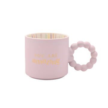 Blush pink ceramic “You Are Amazing” mug with gold lettering, rainbow-striped interior, and bubble handle — motivational boxed mug gift.