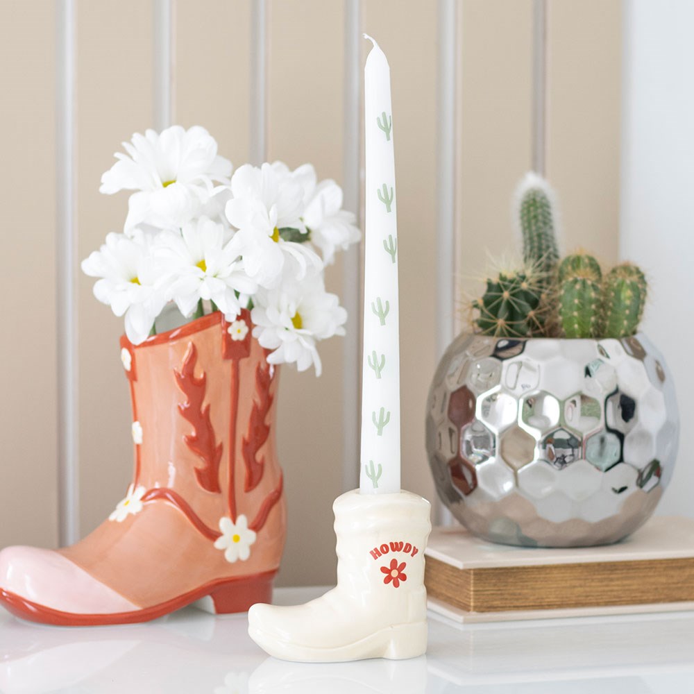 Ceramic cowboy boot candle holder with white cactus taper candle, styled with flowers and cactus décor on tabletop.