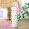 Spring floral print candle with pink tassel and fresh linen fragrance, displayed with green leaves in background.