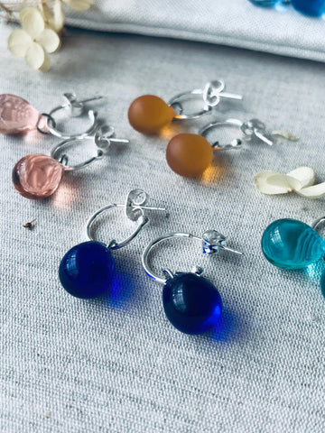 Olive green sea-glass droplet earrings on sterling-silver hoops displayed on linen fabric