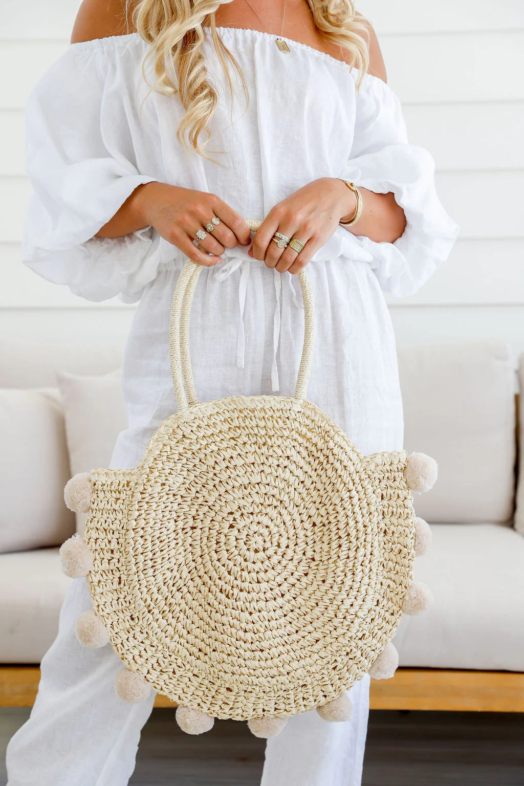 Woman holding natural round straw tote bag with pom pom accents – stylish women’s tote and perfect gift for her