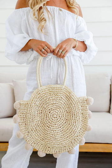 Woman holding natural round straw tote bag with pom pom accents – stylish women’s tote and perfect gift for her