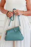 Woman holding an elegant teal frame clutch handbag with gold hardware – women’s bag and perfect gift for her