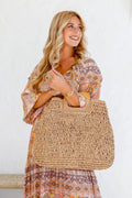 Woman holding a tan woven tote bag with wooden handles – lightweight summer handbag and stylish gift for her