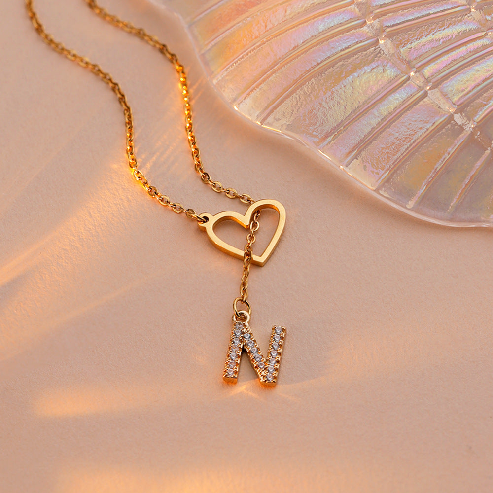 Gold heart and initial necklace worn on model with sparkling letter pendant
